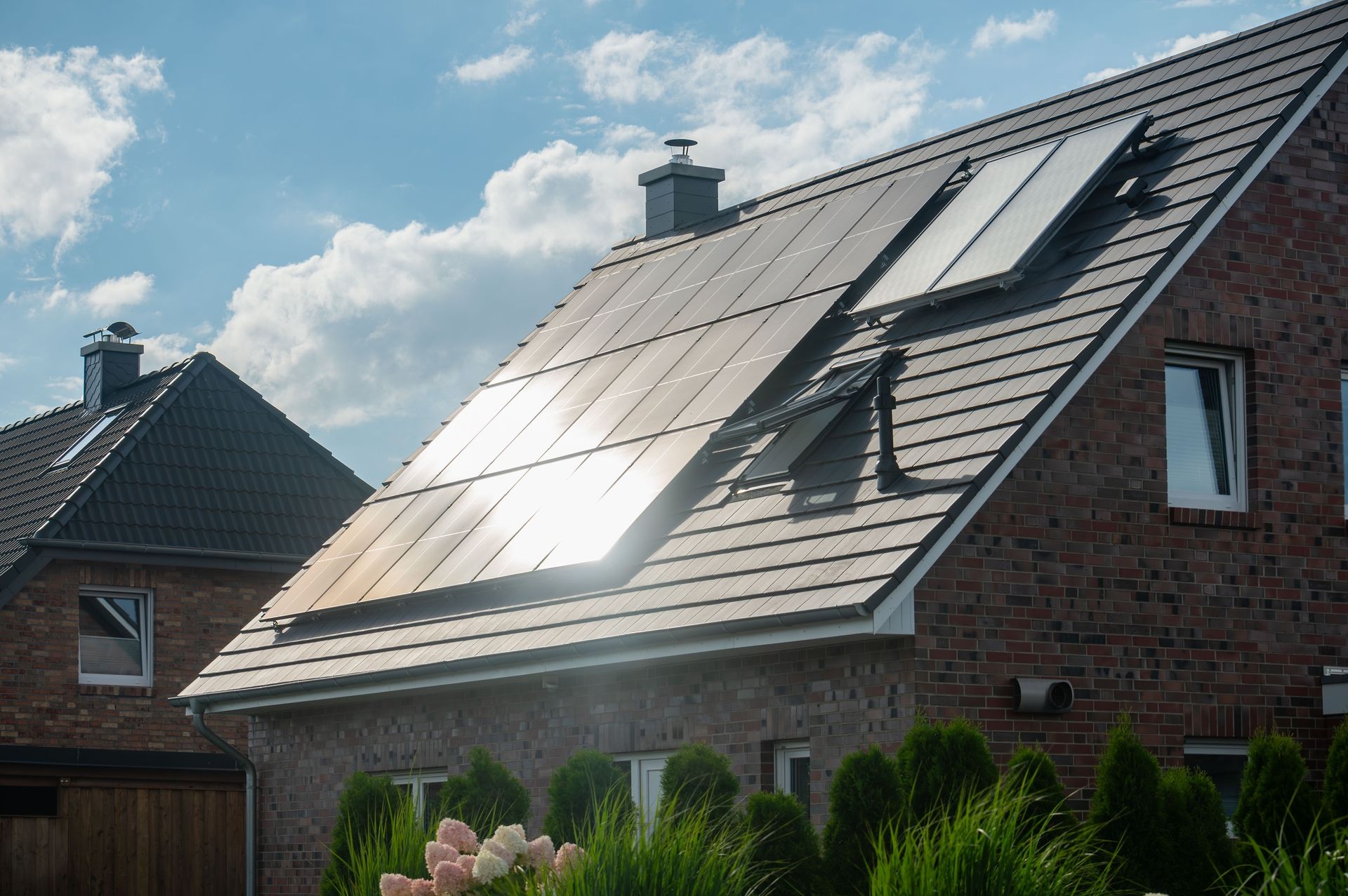 Einfamilienhaus mit Photovoltaikanlage und Solarkollektoren auf dem Ziegeldach bei Sonnenschein